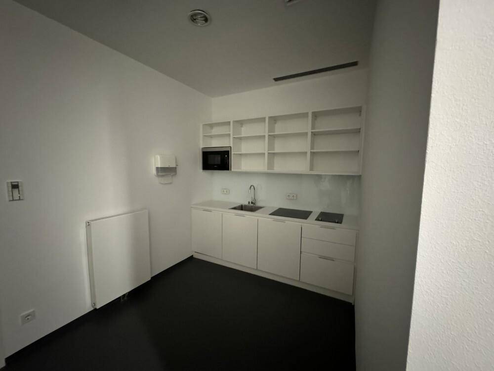 Kleine, moderne Küchenzeile mit weißen Schränken, Spüle, Kochfeld und Mikrowelle in einem hellen Raum.