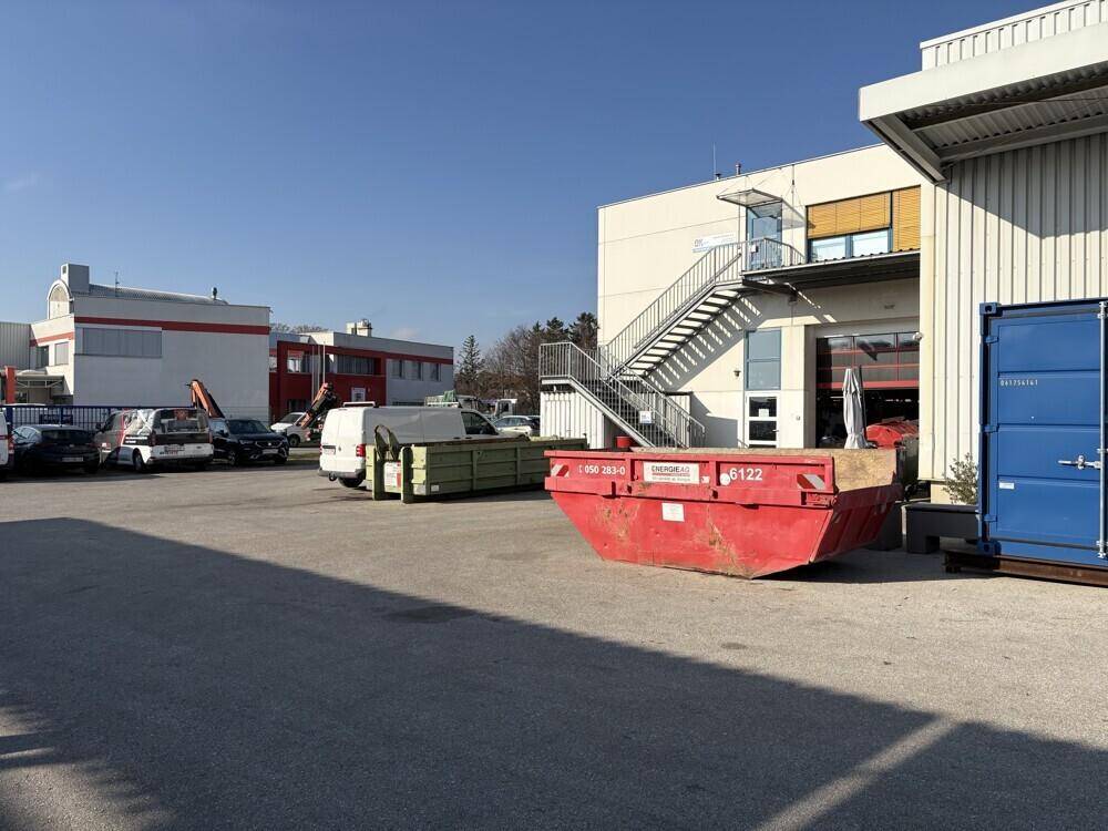 Industriegebäude mit Außentreppe, Ladebereich und einem großen roten Abfallcontainer.