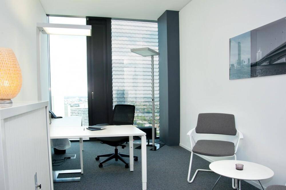 Helles Einzelbüro mit Schreibtisch, Sitzgelegenheit und großem Fenster mit Blick auf die Umgebung.