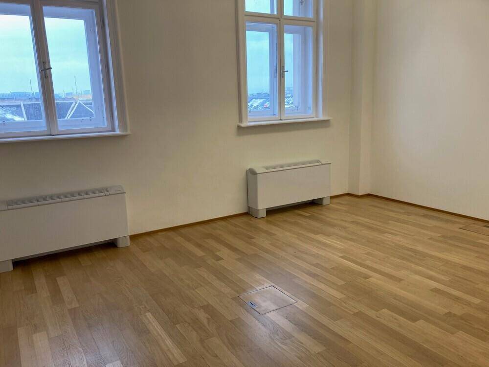 Geräumiges Büro mit Holzboden und zwei großen Fenstern, die viel Tageslicht hereinlassen.