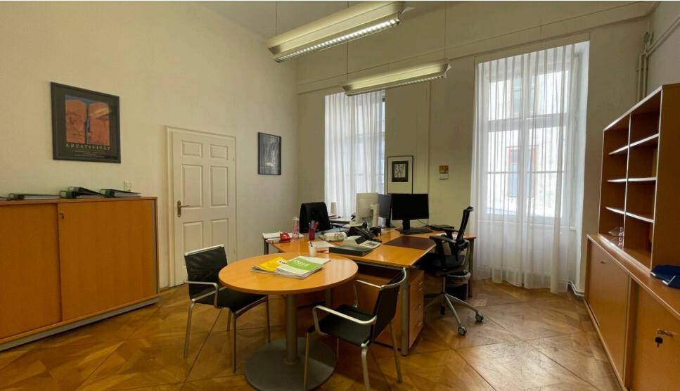 Helles Büro mit klassischem Fischgrätparkett, zwei großen Fenstern und traditionellen Büromöbeln.
