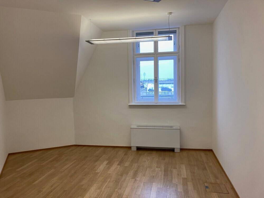 Helles Büro mit Holzboden, Dachschräge und einem großen Fenster mit Stadtblick.