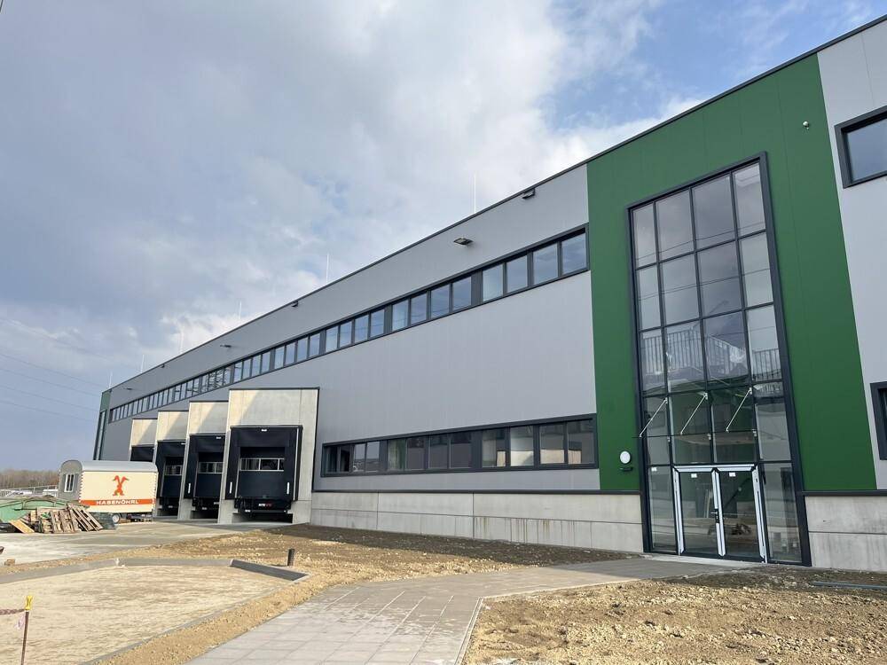Die moderne Fassade des Industriegebäudes mit mehreren Laderampen und einem auffälligen gläsernen Eingangsbereich.