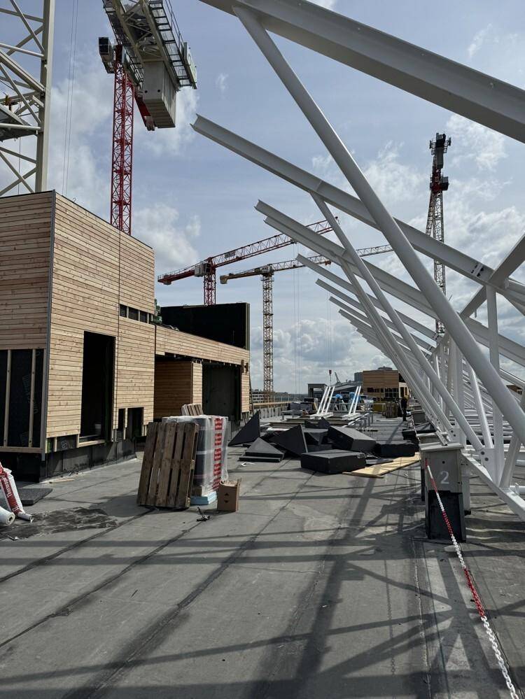 Eine Baustelle auf dem Dach mit Metallstrukturen und Kränen im Hintergrund unter einem bewölkten Himmel.