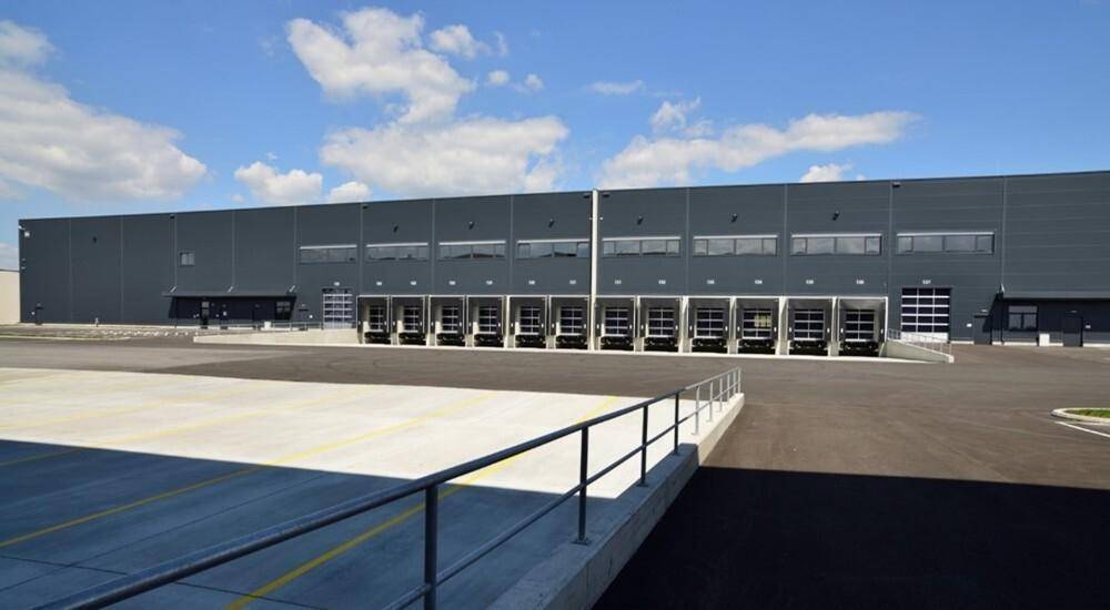 Weitläufige Außenansicht einer Logistikhalle mit vielen Laderampen und großem Vorplatz.