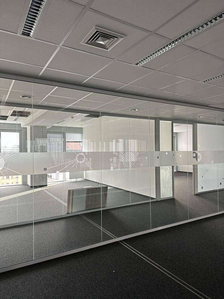 Moderner Bürobereich mit Glaswänden und dekorativen Mustern, der verschiedene Arbeitsbereiche abtrennt.
