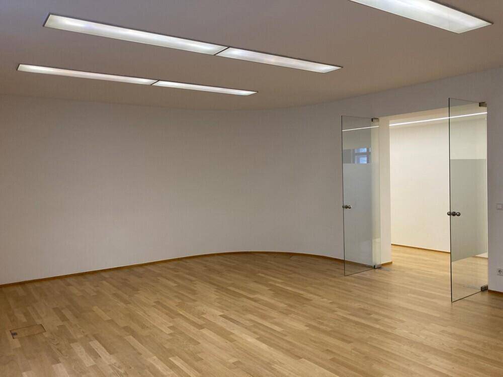 Modernes Büro mit Holzboden, abgerundeter Wand und Glastüren zu einem weiteren Raum.