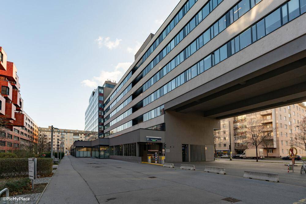 Langes, modernes Bürogebäude mit heller Fassade und überdachtem Eingangsbereich für Fahrzeuge.
