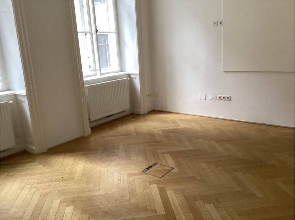 Geräumiges Zimmer mit Fischgrätparkett, großen Fenstern und viel Tageslicht.
