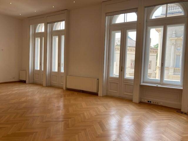 Geräumiger, heller Raum mit Fischgrätparkett, hohen Decken und mehreren hohen Fenstertüren.