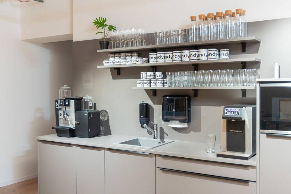 Moderne Teeküche mit Spüle, Kaffeemaschine, Mikrowelle und Regalen für Gläser und Geschirr.