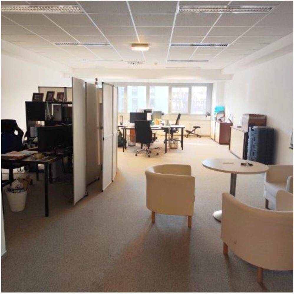 Geräumiger Bürobereich mit Arbeitsplätzen, Trennwänden und einer kleinen Sitzecke, ausgestattet mit Teppichboden.