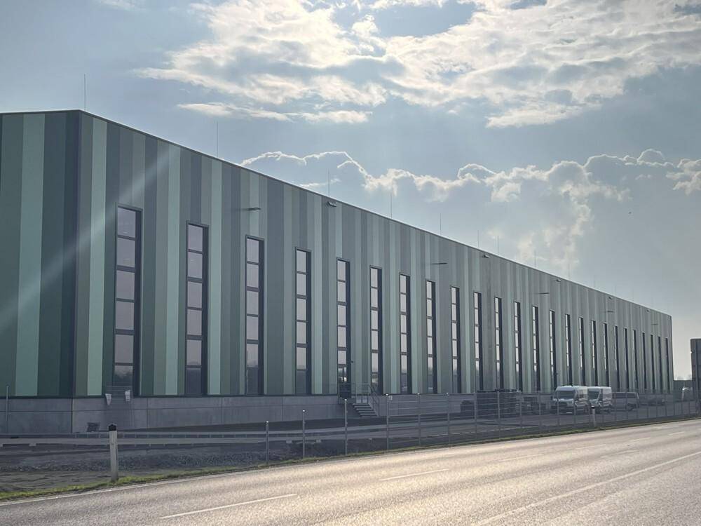 Die Fassade des Industriegebäudes zeigt ein modernes Streifenmuster in verschiedenen Grüntönen mit hohen Fenstern.