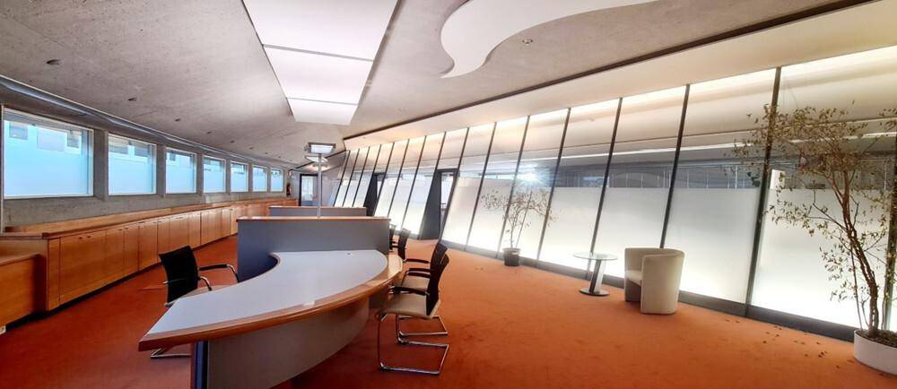 Moderner Empfangsbereich oder Großraumbüro mit geschwungenem Tresen, großen Fenstern und Pflanzen.