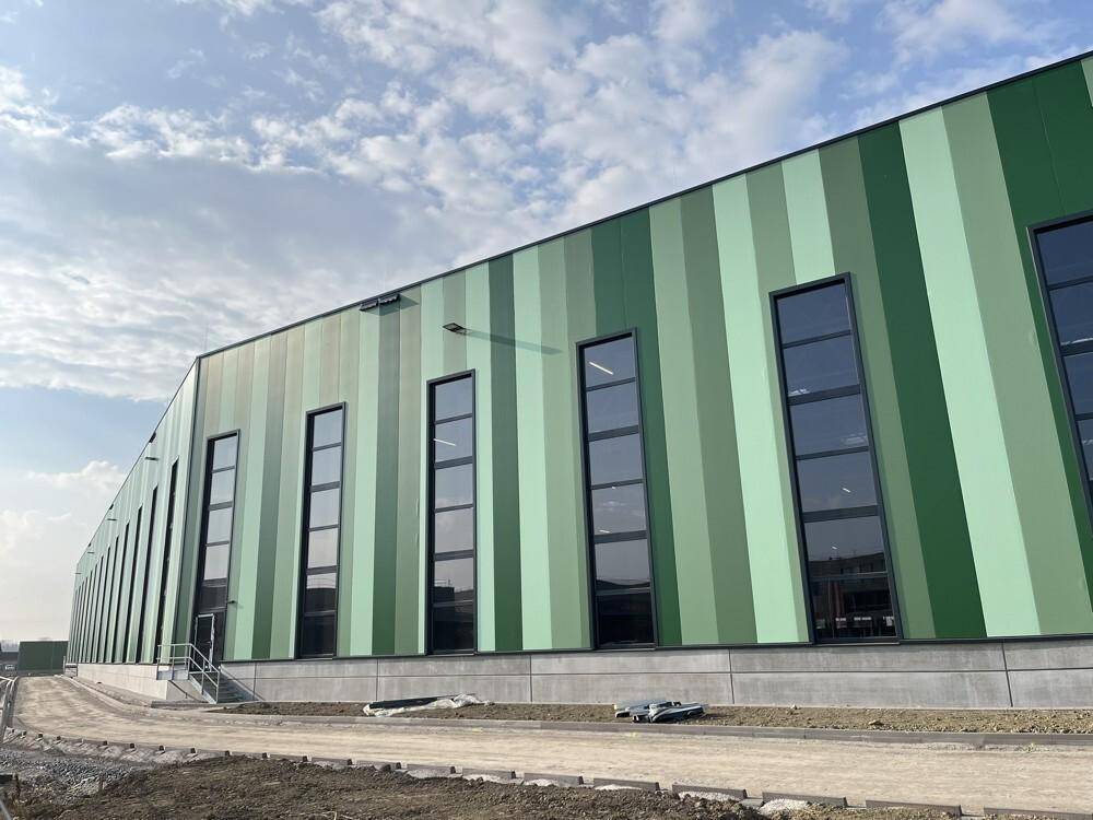 Nahaufnahme der markanten gestreiften grünen Fassade des Industriegebäudes mit hohen, vertikalen Fenstern.