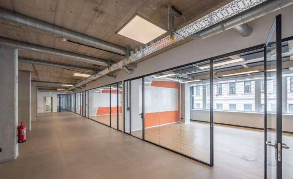 Langer Bürogang mit Glaswänden zu einzelnen Büros und freiliegenden Installationen an der Decke.