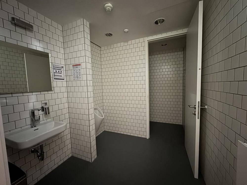 Sauberer Toilettenraum mit weißen Fliesen, Waschbecken und Urinal, in gutem Zustand.
