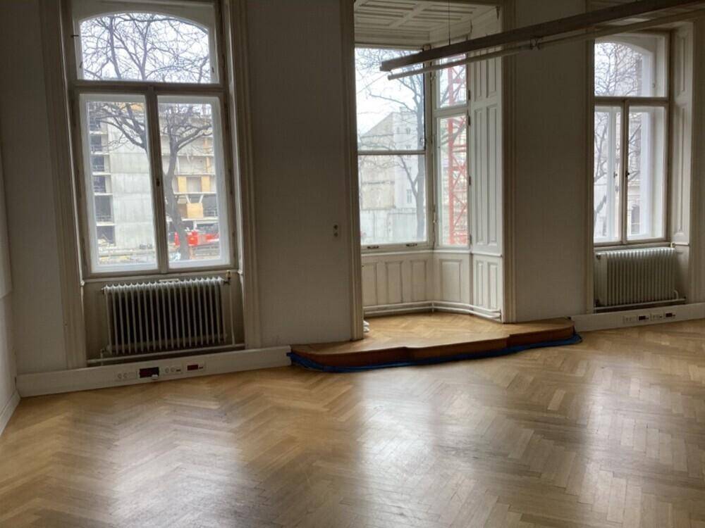 Großes Zimmer mit Parkettboden, mehreren hohen Fenstern und einem Erkerbereich.