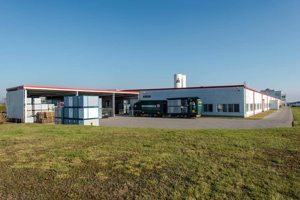 Weitläufiges Industriegelände mit Lagerflächen, einem LKW und grünen Wiesen unter blauem Himmel.