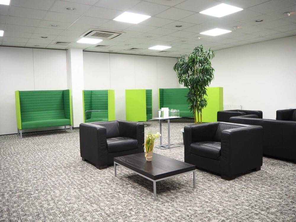 Geräumiger Loungebereich mit schwarzen Ledersesseln, einem Couchtisch und auffälligen grünen Sitznischen.
