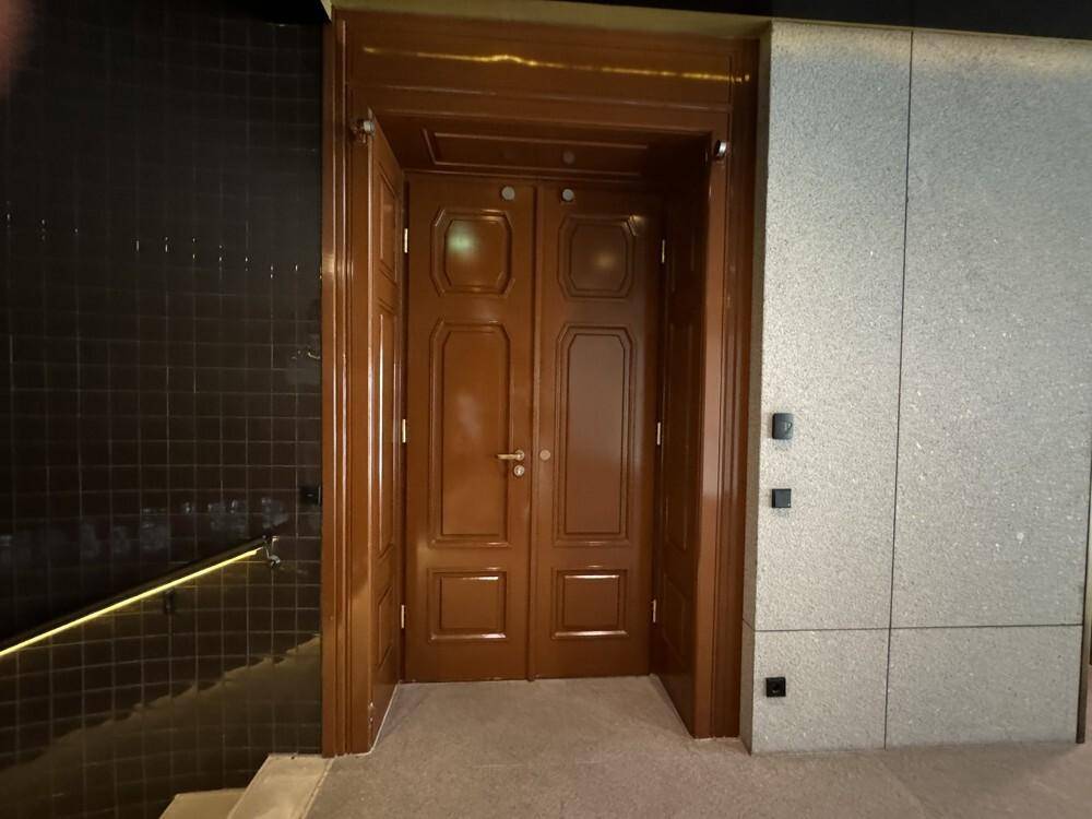 Elegante Holztüren in einem Eingangsbereich mit dunklen Fliesen und hellen Steinwänden.