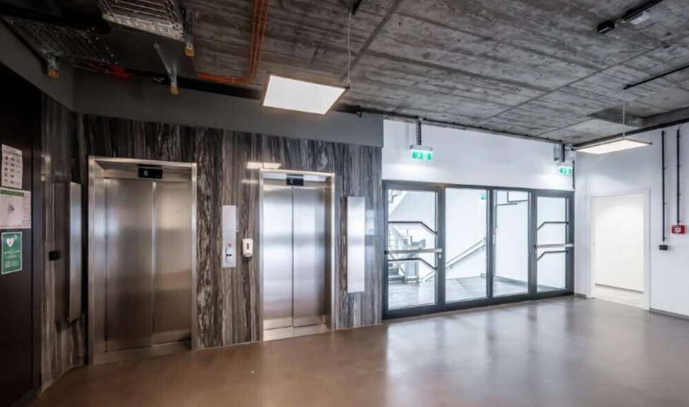 Moderner Eingangsbereich mit zwei Aufzügen, Treppenhaus und Sichtbetondecke im Industriestil.