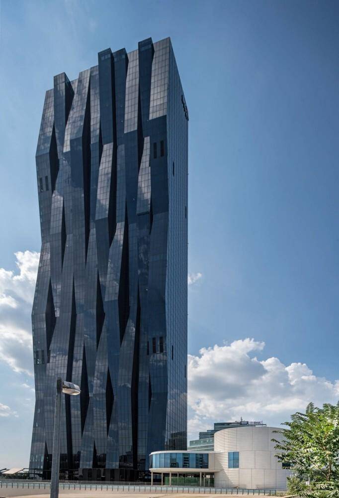 Detailansicht des markanten Wolkenkratzers mit seiner einzigartigen, geometrisch strukturierten Glasfassade unter blauem Himmel.