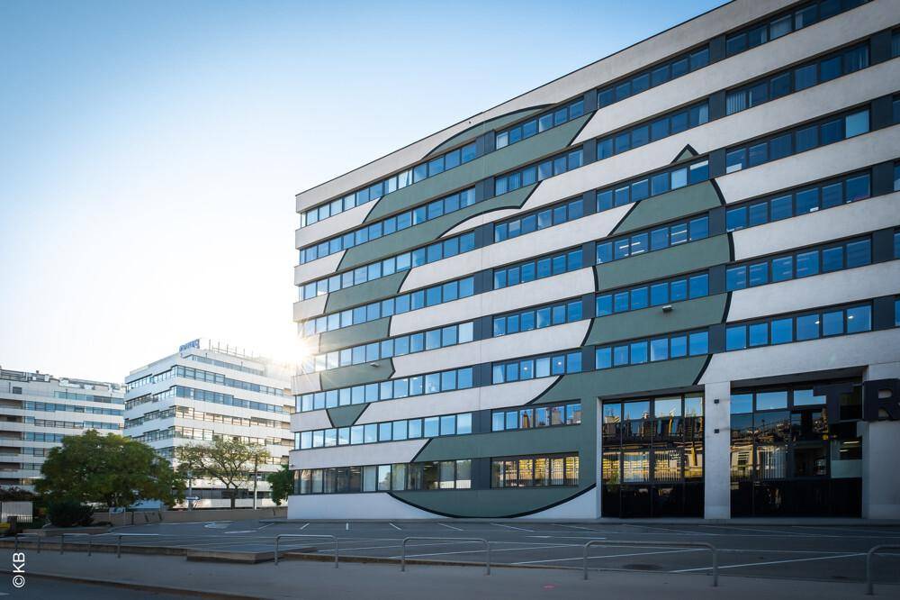 Detailansicht der modernen Gebäudefassade mit geometrischem Muster und vielen Fenstern im Sonnenlicht.