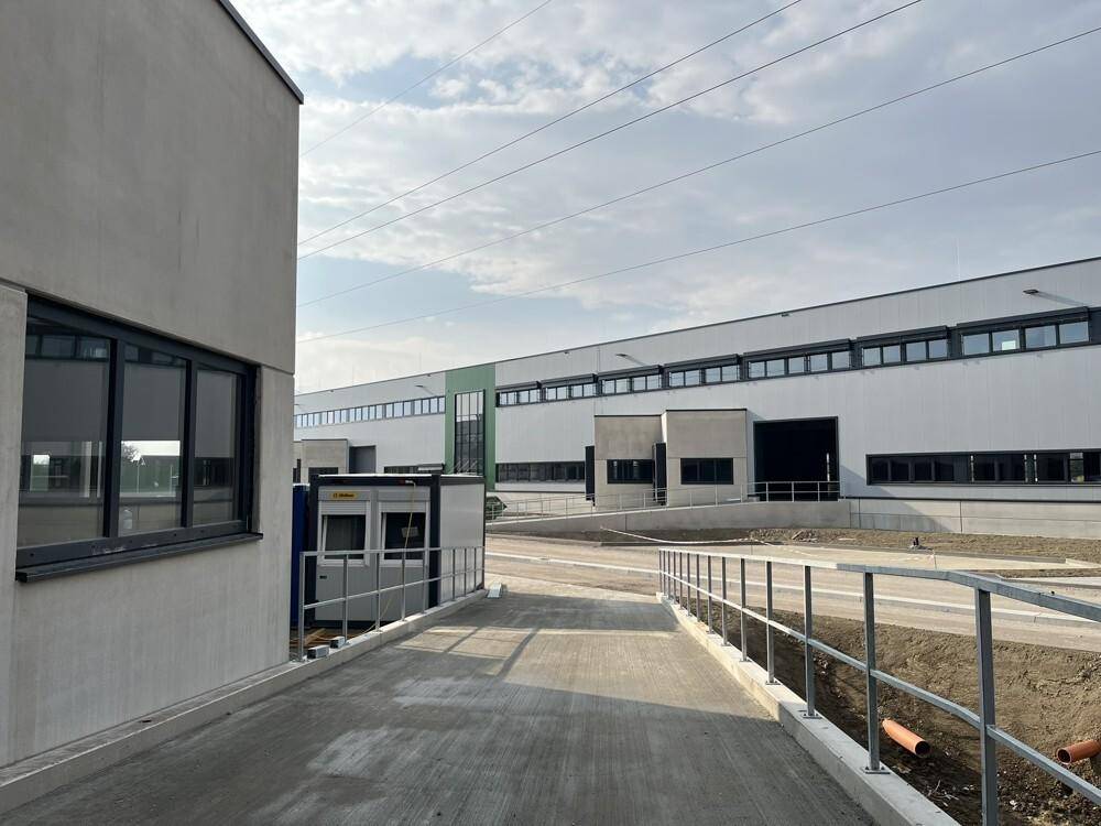 Eine Betonrampe führt zu einem der Gebäude, im Hintergrund sind weitere Gebäudeteile und Stromleitungen zu sehen.