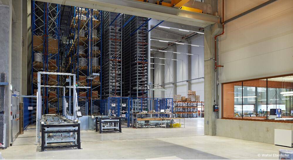 Große Lagerhalle mit Regalsystemen, Arbeitsstationen und einem angrenzenden Bürofenster für die Verwaltung.