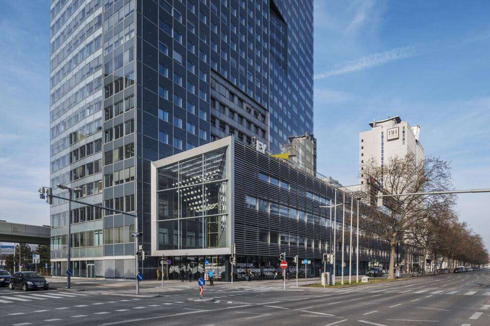 Moderne Hochhausfassade mit angrenzendem Bürogebäude und Glasfront an einer belebten Straße.