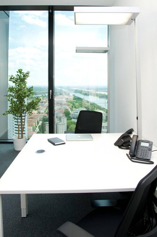 Büroschreibtisch mit Pflanze, Laptop und Telefon, mit Panoramablick auf die Stadt und den Fluss.