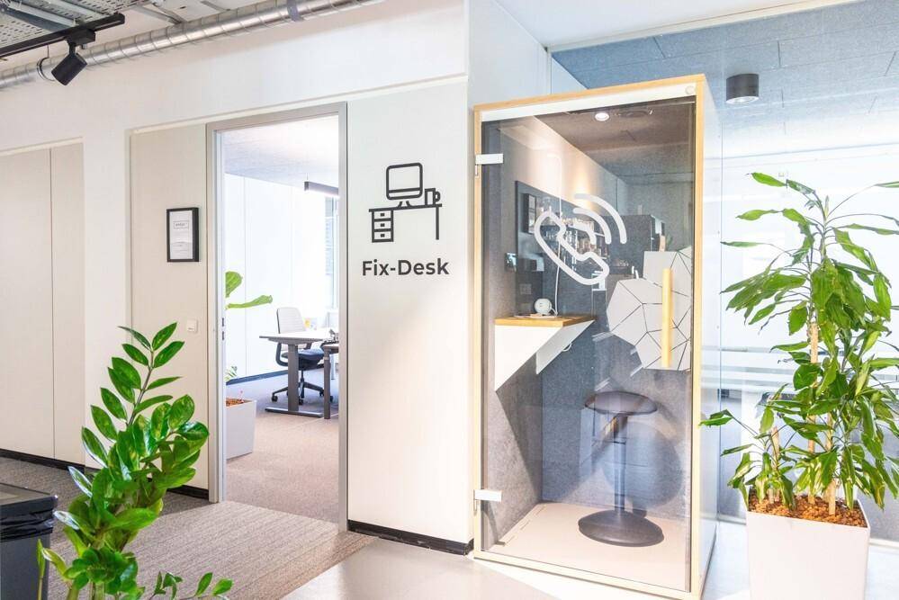 Eingangsbereich eines Büros mit "Fix-Desk"-Beschilderung und einer schallgedämmten Telefonkabine.