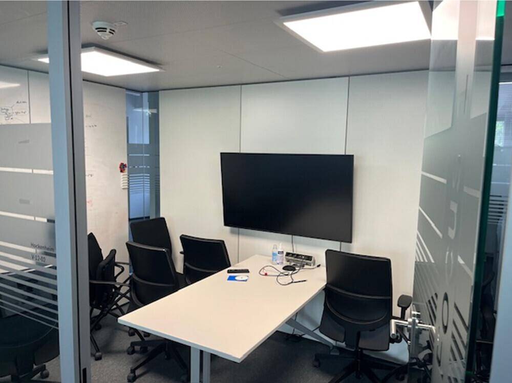 Konferenzraum mit großem Bildschirm, modernem Tisch und bequemen Bürostühlen.