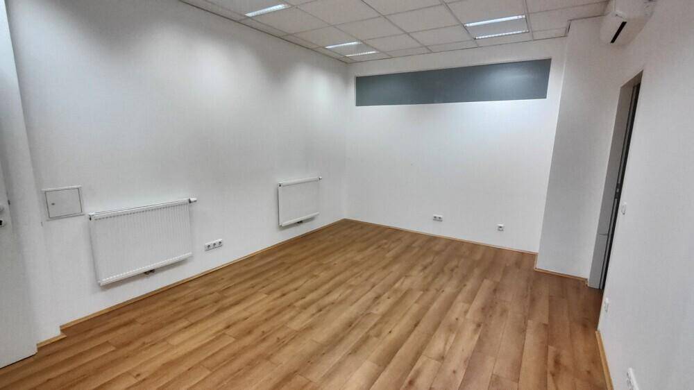 Büroraum mit Holzboden, weißen Wänden und Heizkörpern, ausgestattet mit einer Rasterdecke.