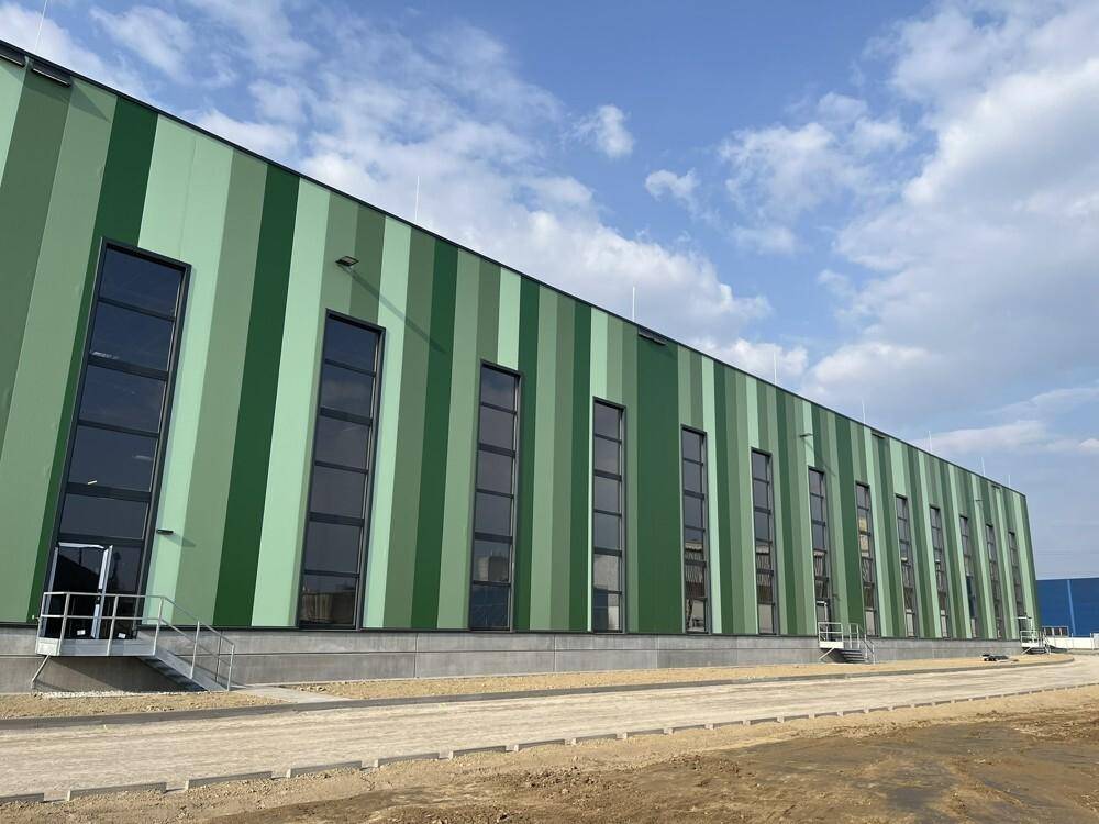 Die gestreifte grüne Fassade des Industriegebäudes mit hohen, schmalen Fenstern unter einem bewölkten Himmel.