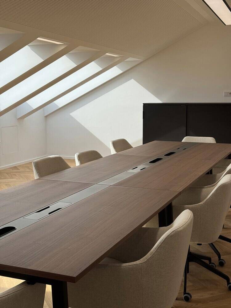 Großer Konferenzraum mit langem Holztisch, bequemen Stühlen und viel Tageslicht durch Dachfenster.
