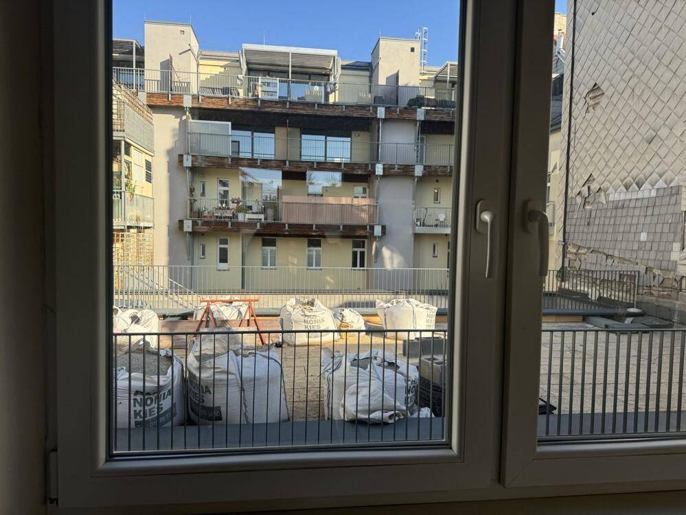 Blick aus dem Fenster auf eine Dachbaustelle mit Materialcontainern und umliegenden Gebäuden.