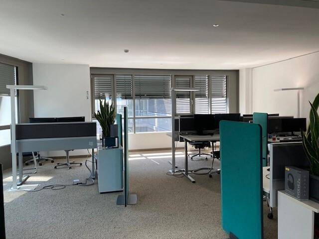 Geräumiges Büro mit Teppichboden, großen Fenstern mit Jalousien und modernen Arbeitsbereichen.
