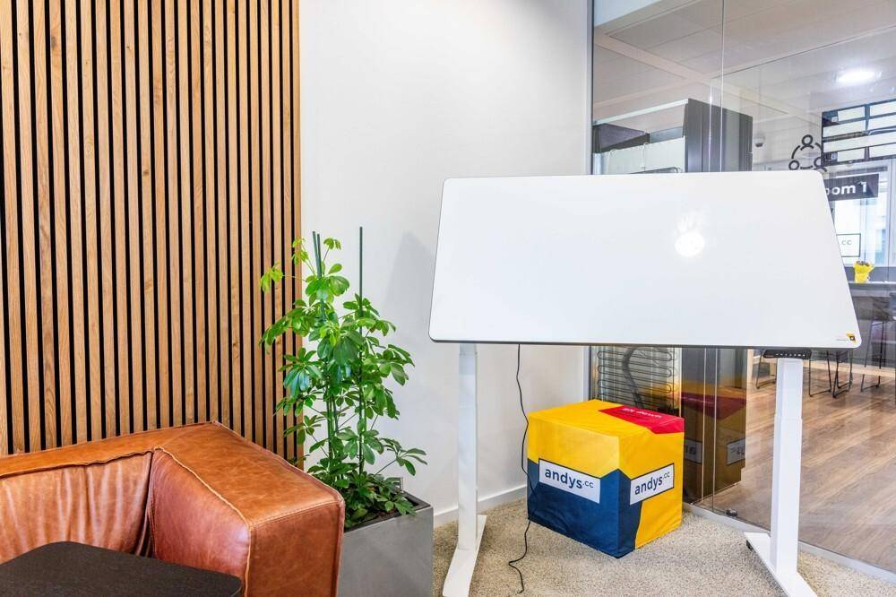 Detailansicht eines Ledersofas, einer Pflanze und eines höhenverstellbaren Schreibtisches mit Laptop.
