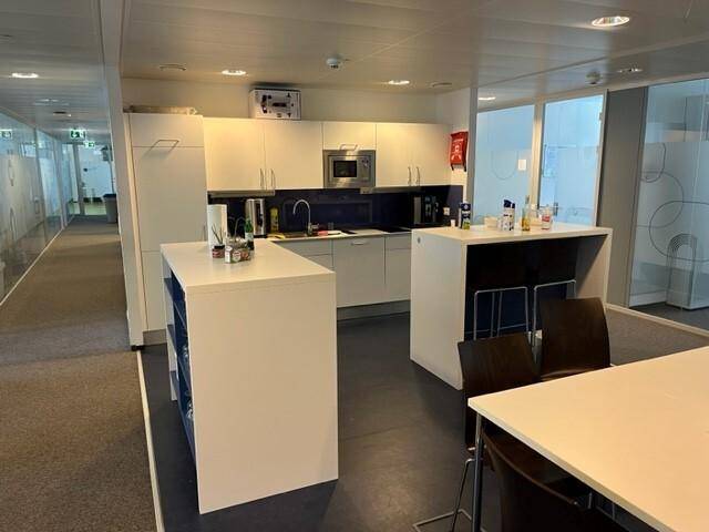 Moderne Büroküche mit weißen Schränken, Mikrowelle und einer Kücheninsel für Pausen.