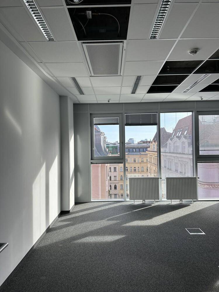 Heller Büroraum mit Teppichboden, großen Fenstern und Blick auf die umliegenden Gebäude.