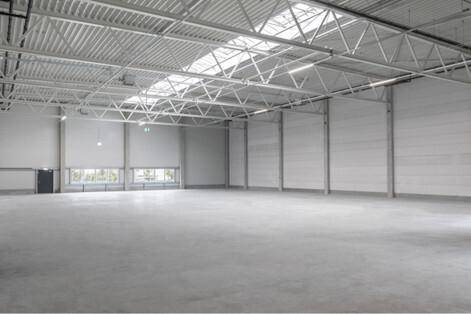Geräumige, leere Lagerhalle mit hohen Decken, sichtbaren Trägern und Oberlichtern für Tageslicht.