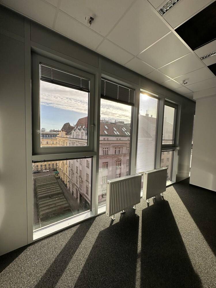 Heller Büroraum mit Teppichboden, großen Fenstern und Blick auf die Stadt.