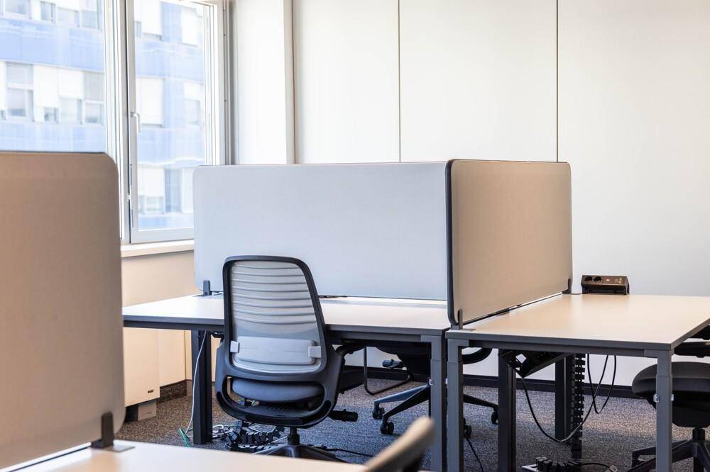 Arbeitsplätze in einem modernen Büro mit Trennwänden und ergonomischen Bürostühlen am Fenster.