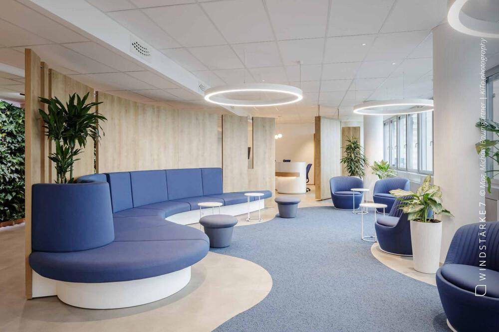 Moderner Loungebereich mit blauen Sofas, Pflanzen und geschwungenen Designelementen.