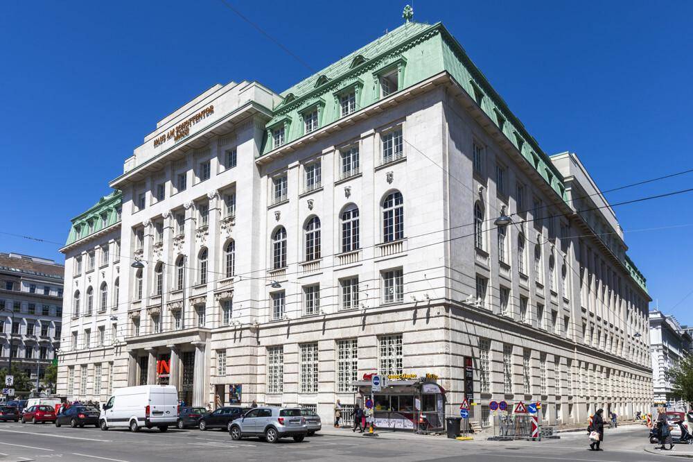 Historisches Gebäude mit beeindruckender Architektur, vielen Fenstern und einem markanten grünen Mansarddach an einer belebten Straße.