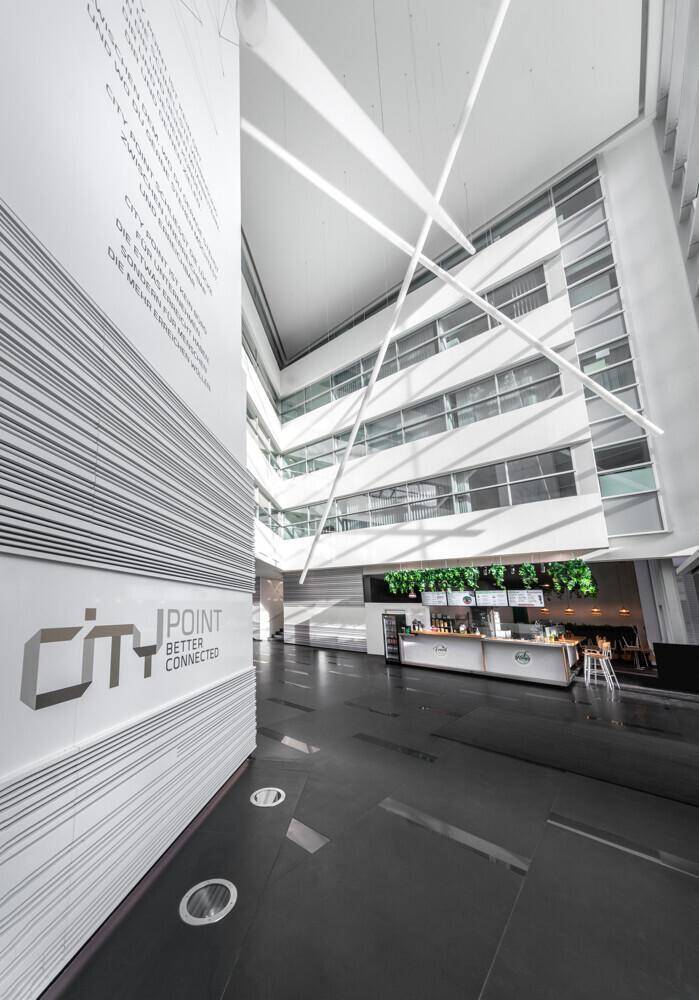 Geräumige, moderne Lobby mit sehr hohen Decken, einem Cafébereich und stilvoller Beleuchtung.