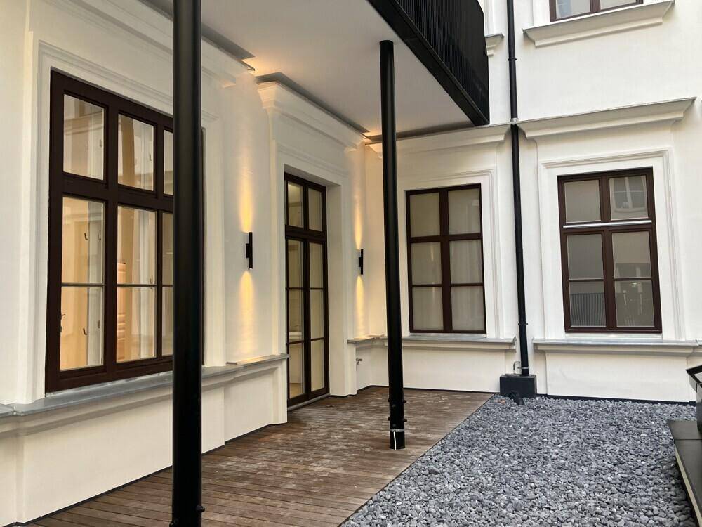 Attraktiver Innenhof mit Holzterrasse, modernen Wandleuchten und großen Fenstern zum Gebäude.