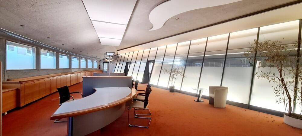 Empfangsbereich mit geschwungenem Tresen, großen Fenstern und orangefarbenem Teppichboden.